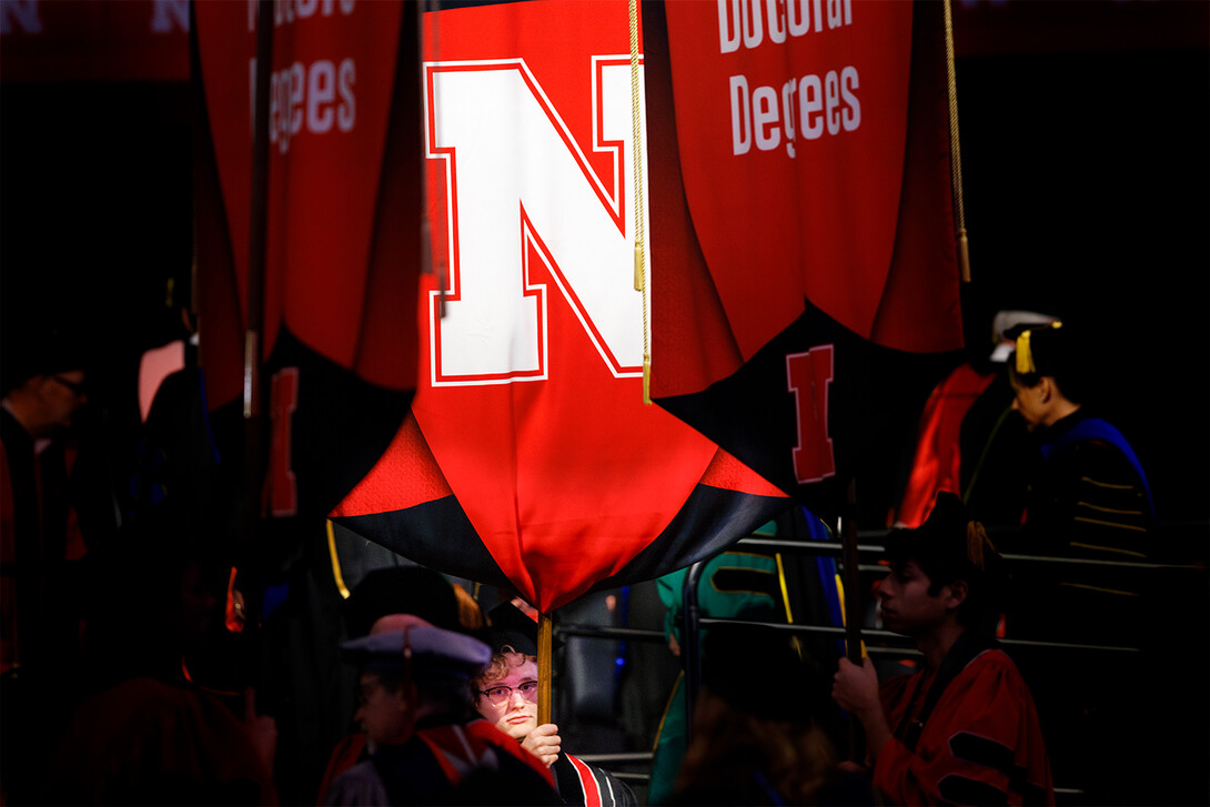 A spotlight shines on Paul Pechous as he holds a red banner featuring the Nebraska N in white