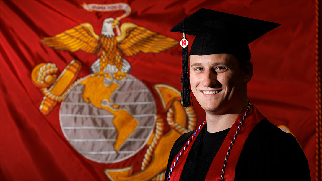 L.J. Bird in commencement regalia with U.S. Marine Corps flag in background