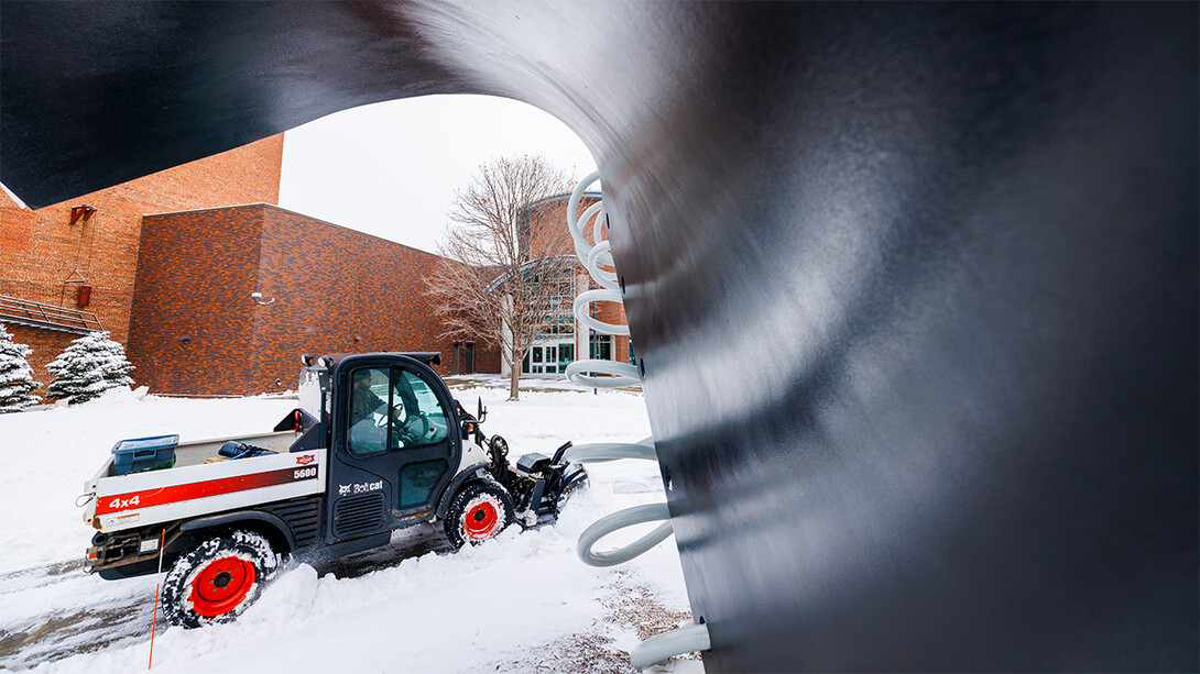 Foregrounded by the Torn Notebook sculpture, a Bobcat vehicle clears snow from a sidewalk