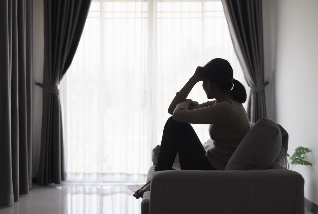 A woman in silhouette sits on a sofa and appears to be pensive.