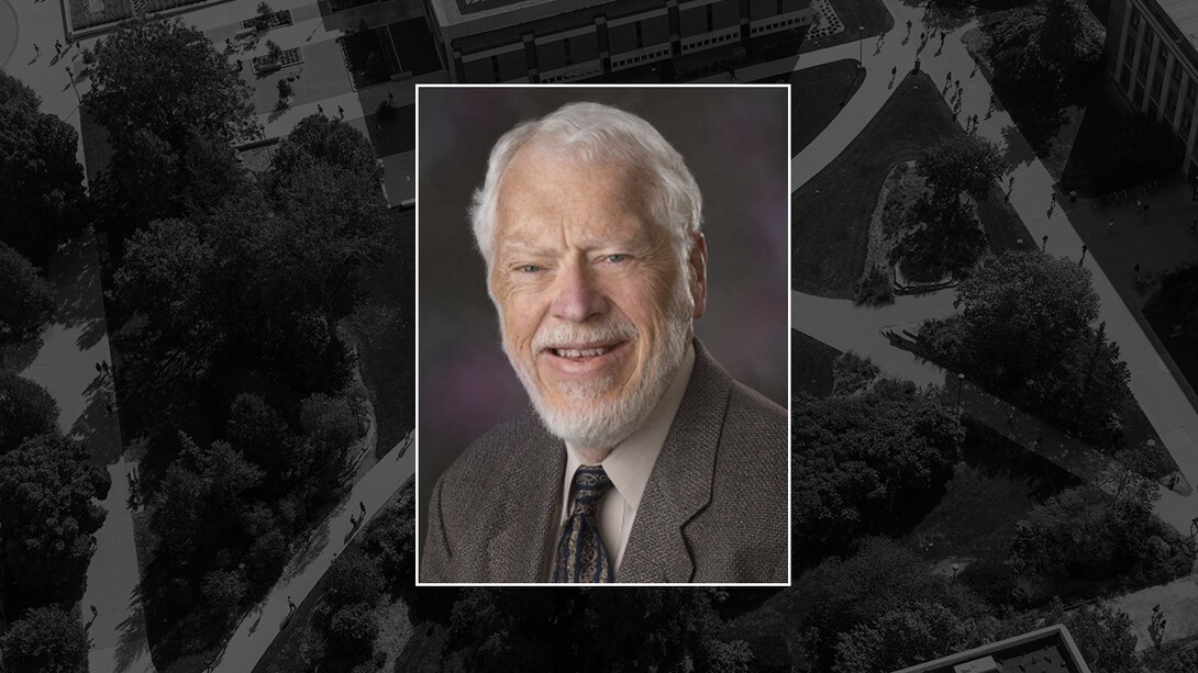 Dr. James Specht, a white man with white hair and a beard, a long face, smiles in a grey suit.