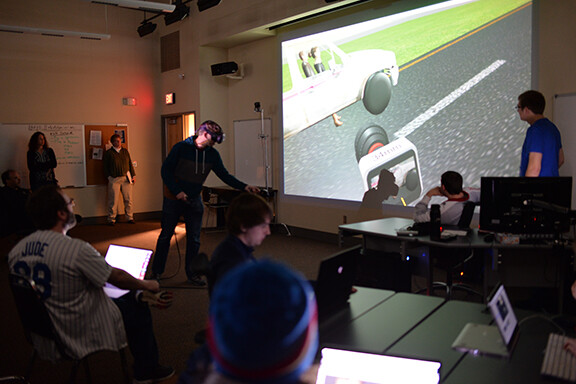 Ben Hartzell (left, in virtual reality goggles), a senior film and new media major, shows the progress of his team's final project in class on April 10.