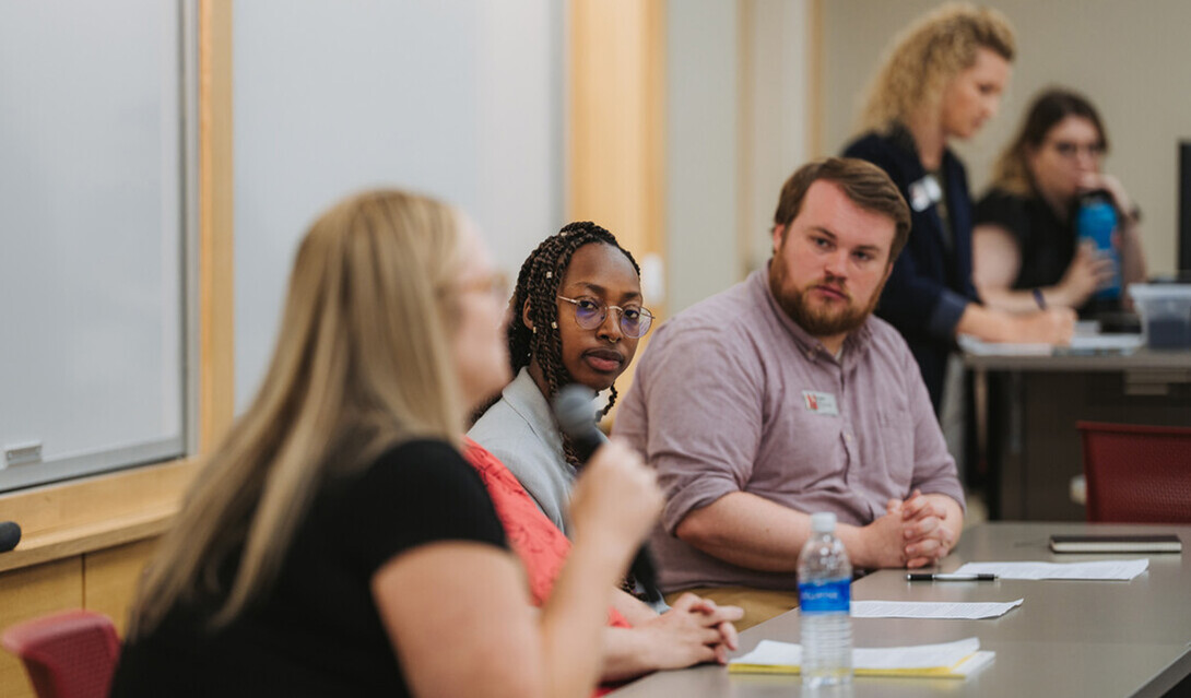 Someone speaks into a microphone as two colleagues listen.