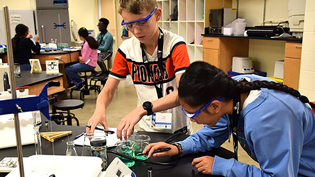 Two middle school students examine beakers of green liquid.