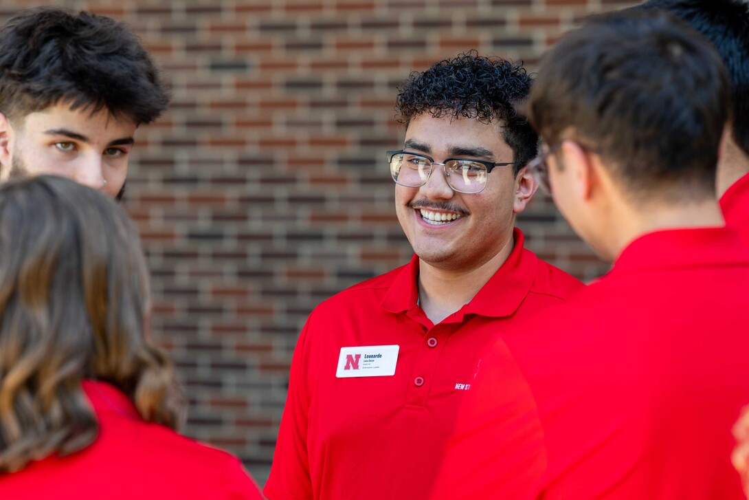 Leonardo Luna-Duran wears glasses and red collared tee shirt while chatting with fellow New Student Enrollment leaders.