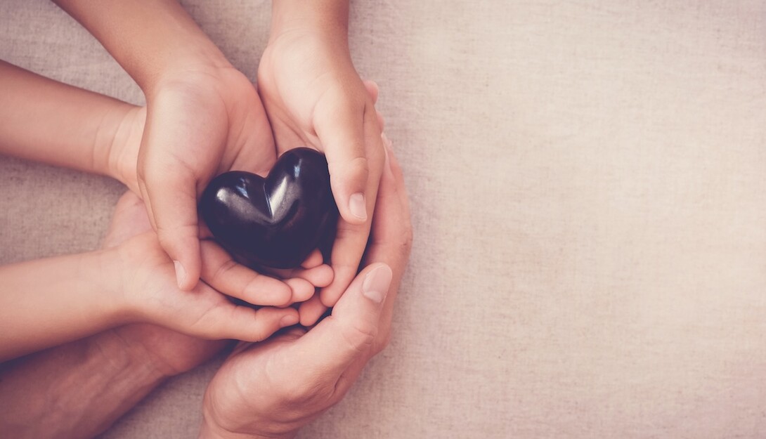 multiple hands clasped together, holding a black heart