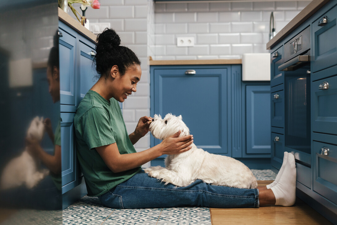 A woman smiles as she plays with her dog in the kitchen