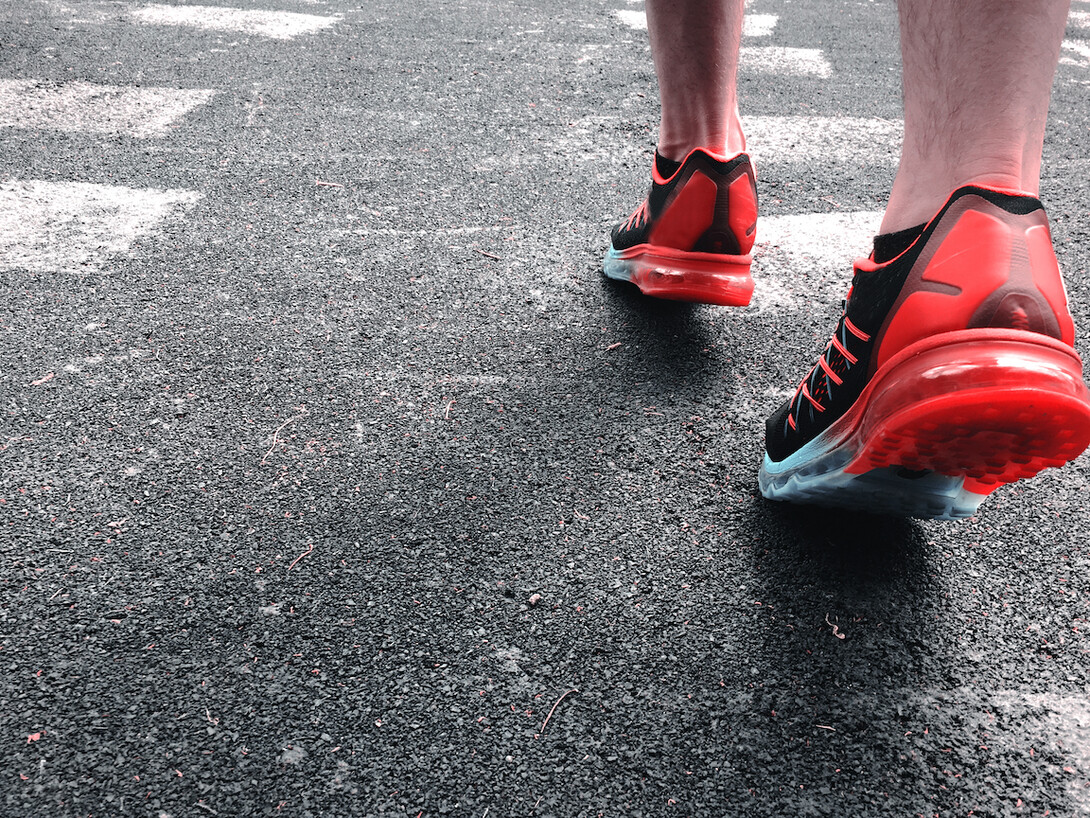 A person wearing red tennis shoes walking on concrete pavement